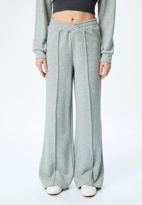 Lichtgrijze, wijde sweatpants van zacht materiaal met een gestructureerde tailleband en plooien aan de voorkant, die een ontspannen silhouet bieden.