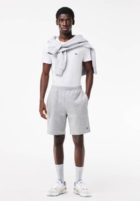 Gray sweat shorts with elastic waistband, white fitted t-shirt, and light gray sweatshirt draped over shoulders, paired with white sneakers.