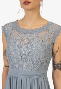 Vestito di pizzo azzurro chiaro con motivo floreale, scollatura ondulata e tessuto morbido. Caratterizzato da una vita plissettata e maniche corte.