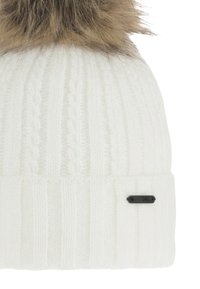 White knit beanie with ribbed texture, featuring a plush tan fur pom-pom on top and a small black tag at the side.