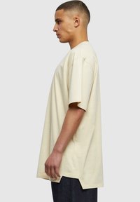 Tricou bej supradimensionat, cu mâneci scurte, decolteu rotund, din material de bumbac, având slituri laterale la tiv pentru un plus de stil și confort.