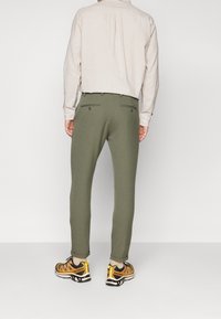 Olivgröna byxor med smal passform, med två bakfickor och en slät yta, kombinerade med svarta och gula träningsskor.