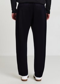 Marineblaue Hose mit geradem Schnitt, ausgestattet mit zwei Gesäßtaschen und einem elastischen Bund. Der Stoff hat eine glatte Textur und wird mit weißen Schuhen kombiniert.