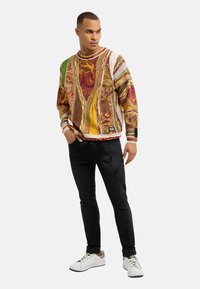 Sweatshirt à motifs multicolores avec manches longues, col rond et poignets côtelés, associé à un jean slim noir et des baskets blanches.