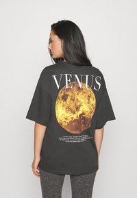 Dark gray oversized t-shirt featuring a large yellow and orange planet graphic with "VENUS" text above and a definition below. Soft fabric.