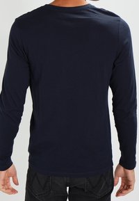 Marineblaues Langarmshirt aus weichem, glattem Stoff; mit Rundhalsausschnitt und anliegenden Ärmeln, in einem schlichten, klaren Design.