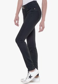 Pantalones vaqueros negros ajustados de cintura alta, con dos botones en la parte frontal, bolsillos delanteros y traseros, y una textura de denim suave. Combinados con zapatillas blancas.