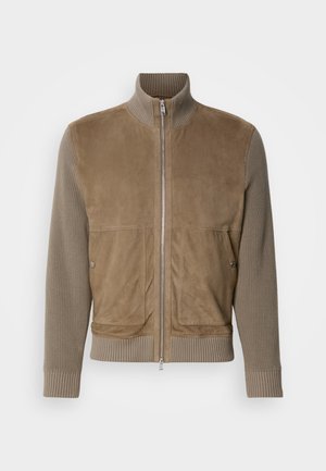 Veste en cuir suédine beige avec un corps en tricot côtelé, un col montant, une fermeture zippée à l'avant et deux grandes poches avant. Texture lisse avec des matériaux contrastants.