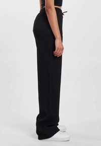 Black ribbed wide-leg pants with an elastic waistband and drawstring. Styled with white sneakers, showcasing straight silhouette.