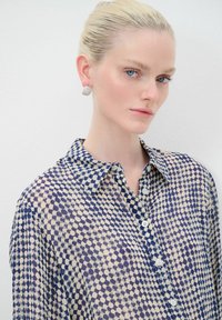 Camicia button-up con un motivo a pois geometrici in navy e crema. Presenta un colletto classico e un tessuto leggero e trasparente.