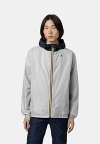 Giacca a vento grigio chiaro con cappuccio blu navy; presenta una zip completa, righe orizzontali e polsini elasticizzati. Logo sul petto.