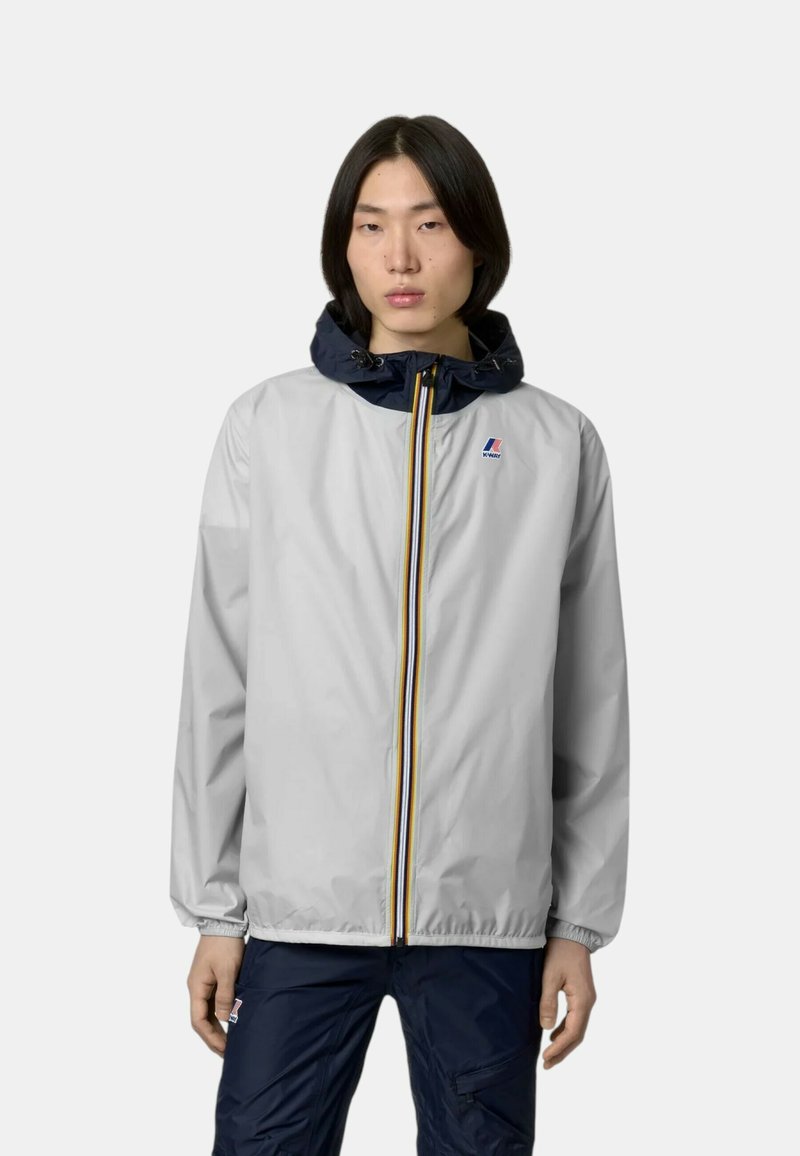 Giacca a vento grigio chiaro con cappuccio blu navy; presenta una zip completa, righe orizzontali e polsini elasticizzati. Logo sul petto.