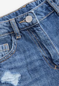 Pantaloni corti in denim blu con una toppa strappata, dotati di un bottone argentato e cuciture in contrasto lungo il girovita e le tasche.