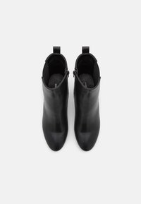 Musta nahkainen nilkkuri, jossa on virtaviivainen siluetti, terävä kärki ja minimalistinen muotoilu sekä vetokahva takana.