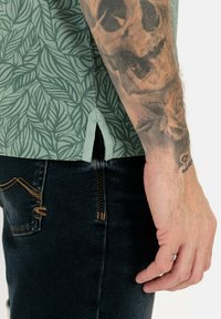 Kortom mouw shirt in lichtgroen met een bladerenpatroon; heeft een geventileerde zoom en is gecombineerd met donkere spijkerbroeken met contrasterende stiksels.