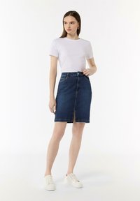 Denim Bleistiftrock mit Schlitz vorne, hoher Taille und klassischer Naht. Kombiniert mit einem weißen T-Shirt und cremefarbenen Sneakern.