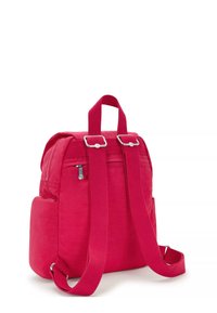 Zaino in tessuto rosso con spalline regolabili, manico superiore e tasca frontale con zip. Presenta una tasca laterale e cuciture lineari.