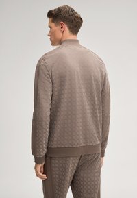 Braune Bomberjacke mit einem subtilen floralen Muster, gerippten Bündchen und Kragen. Weicher Stoff mit lockerer Passform, kombiniert mit passenden Hosen.
