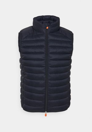 Veste sans manches matelassée noire avec col montant et fermeture éclair avant avec tirettes orange, présentée sur fond blanc.