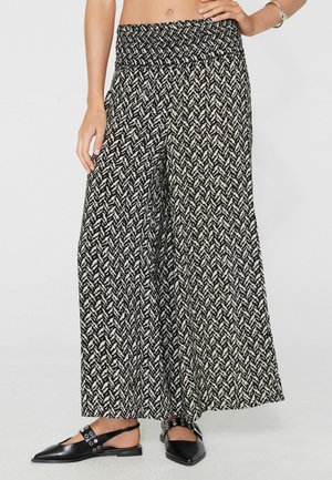 Pantalones de cintura alta y pierna ancha con estampado en blanco y negro combinados con bailarinas negras de punta con tiras traseras y detalles de ojales plateados.