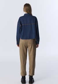 Jeansjack met een cropped ontwerp, contrasterende stiksels; gecombineerd met beige nep-suède broek en zwarte platformlaarzen.