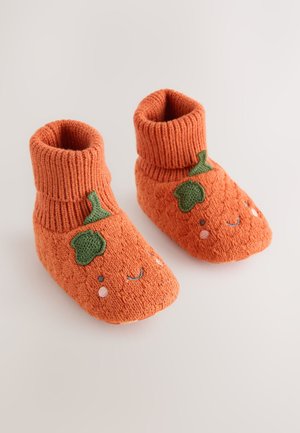Pomarańczowe dziergane buciki dla niemowląt z prążkowanymi mankietami, ozdobione zielonymi liśćmi i haftowanym uśmiechniętym obliczem, zaprojektowane z myślą o komforcie i cieple.