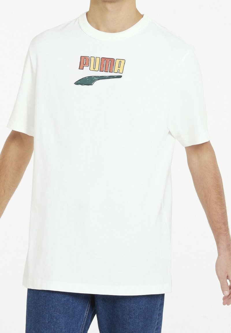 T-shirt en coton blanc avec un logo "PUMA" multicolore et un graphisme vert, col rond et manches courtes, associé à un jean bleu.