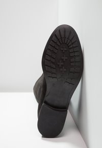 Czarne zamszowe botki za kostkę z teksturowaną gumową podeszwą, charakteryzujące się wytrzymałym wzorem bieżnika oraz płaską, gładką częścią noska. Zaznaczony rozmiar 37.