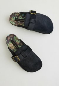 Sorte suede klapfodder med en bred rem, gylden spænde og blomsterpræget indersål. Blød tekstur og rund tå-design for komfort.