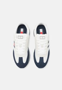 Weiße und marineblaue Sneaker mit einem Obermaterial aus Wildleder und Textil, Schnürdesign, mit einem Logo auf der Zunge und seitlichen Streifen.