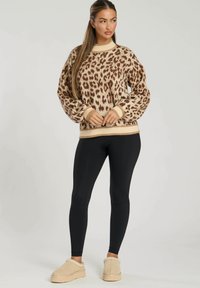 Maglione a maglia con stampa leopardata in beige e marrone, dotato di un collo alto e polsini a coste, abbinato a leggings neri e calzature beige.