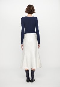 Maglietta a maniche lunghe blu navy abbinata a una gonna midi argento, con una forma svasata e cuciture visibili, completata da stivali neri alti fino al ginocchio.
