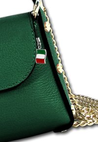 Groene leren handtas met een flapafsluiting, gouden schouderband en een klein Italiaans vlaggetje als accentdetail.
