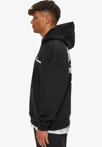 Hoodie noir avec une poche avant, présentant un logo sur la poitrine et un grand graphique au dos. Fabriqué en tissu doux avec des poignets en côte.