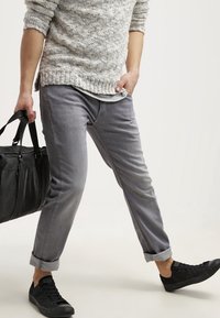 Pantalones de mezclilla gris con un corte relajado, que presentan puños doblados, una textura suave y costuras detalladas, combinados con zapatillas negras y una bolsa tote.