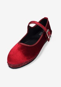 Chaussure Mary Jane en velours rouge avec un bout arrondi, une bride autour de la cheville, une boucle en argent et une semelle en caoutchouc noir. Texture lisse et design simple.