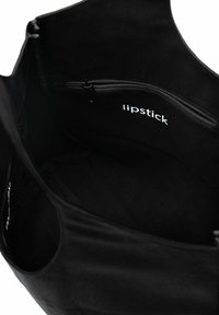 Czarna torba na ramię z gładką teksturą, z zamykaną na zamek kieszenią i białym napisem "lipstick" wewnątrz. Prosty, funkcjonalny design.