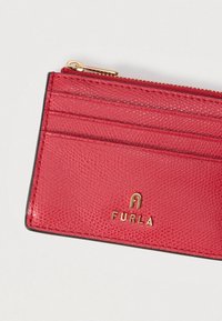 Rød læder kortholder med struktureret finish, med tre kortholdere og en lynlåslomme, prydet med en gylden "FURLA"-logo.