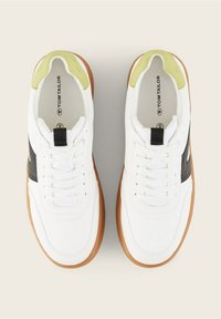 Baskets blanches avec des accents vert clair au talon, des bandes latérales noires, des semelles marron et des lacets blancs, vues de dessus sur un fond neutre.