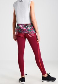 Bordo legíny s bočními oranžovými pruhy, kombinované s květinovým síťovaným topem a šedým zkráceným tílkem bez rukávů. Celý outfit doplňují černé tenisky.