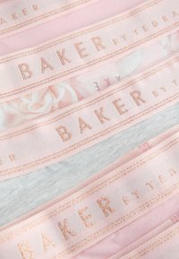 Gros plan sur des bandes de tissu aux motifs pastel rose, gris et floral, avec "BAKER by TED" brodé en fil rose doré.