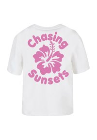 Bijela pamučna majica s velikim dizajnom ružičaste hibiskus cvijeta i izrazom "Lov na zalaske sunca" u podebljanom ružičastom pismu na leđima.