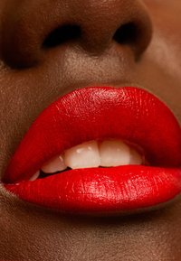 Bright red lips with a smooth, matte finish, revealing white teeth beneath. Rich brown skin tone contrasts with the vibrant lip color.