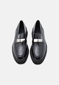 Μαύρα δερμάτινα loafers με γυαλιστερό φινίρισμα, που διαθέτουν οριζόντια μεταλλική λεπτομέρεια στην επάνω πλευρά και πάτο με παχύ υφή.