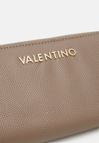 Portofel din piele maro cu o suprafață texturată. Prezintă un logo auriu „VALENTINO” și un închidere cu fermoar.