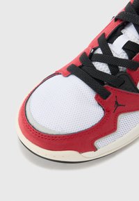 Scarpa sportiva rossa e bianca con tessuto a rete, suola in gomma, lacci neri e dettaglio del logo distintivo sul lato. Design della punta arrotondata.