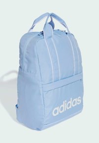 Mochila de color azul claro con dos asas superiores, rayas blancas y un bolsillo frontal. Presenta el logotipo de "adidas" en letras blancas en negrita en la parte inferior del frente.