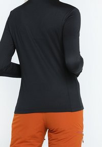 Maglietta nera a maniche lunghe con un design aderente, realizzata in tessuto morbido, con collo alto e cuciture a vista, abbinata a pantaloni arancioni.