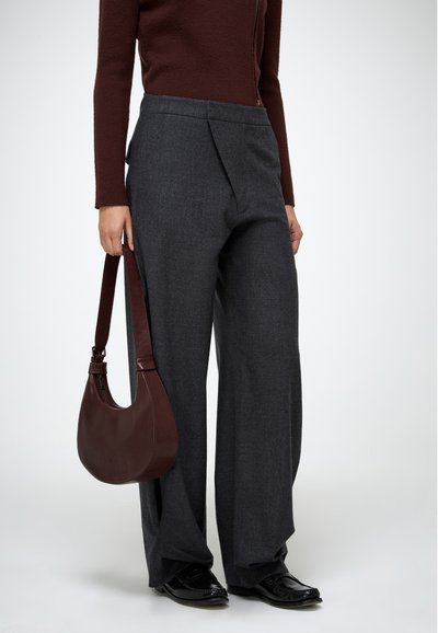 Hallid hallid püksid, millel on volditud esiosa, koos pruuni sobiva toppi ja pruuni nahast õlakotiga, kantud mustade kingadega.