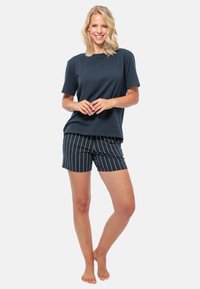 Marineblauw katoenen T-shirt met korte mouwen, gecombineerd met zwart-witte gestreepte shorts. De outfit heeft een relaxed fit en een zachte textuur.
